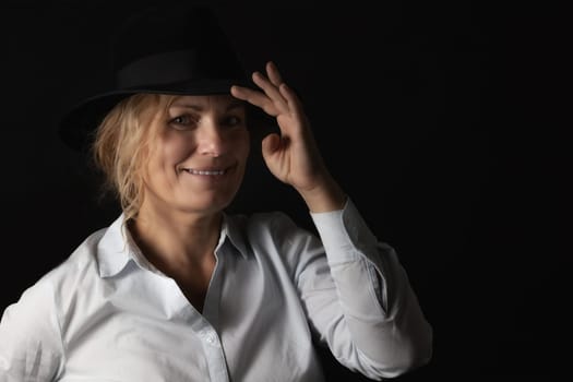 Low key portrait of  smiling  middle age woman holding her black hat.