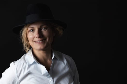 Low key portrait of smiling middle age woman wearing a black hat.
