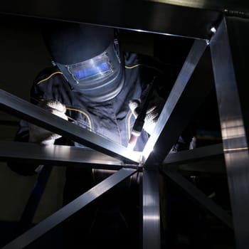A welder works diligently on a metal structure, focusing on precision and safety in an industrial workshop setting after sunset.