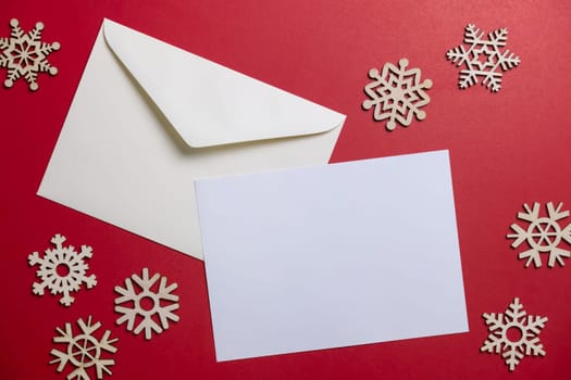Christmas winter festive ornament. Blank paper card and envelope with wooden snowflake on red background. Minimal decoration. Invitation Christmas holiday party. Flat lay, top view, copy space.