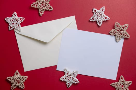 Christmas winter festive ornament. Blank paper card and envelope with wooden decoration on red background. Minimal decoration. Invitation Christmas holiday party. Flat lay, top view, copy space.