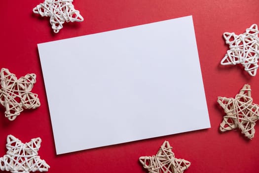 Christmas winter festive ornament. Blank paper card with wooden decoration on red background. Minimal decoration. Invitation Christmas holiday party. Flat lay, top view, copy space.