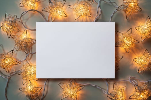 Christmas winter festive ornament. Blank paper card  and Christmas lights decoration background. Invitation Christmas holiday party. Flat lay, top view, copy space.
