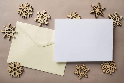 Christmas winter festive ornament. Blank paper card with wooden snowflake on brown background. Minimal decoration. Invitation Christmas holiday party. Flat lay, top view, copy space.