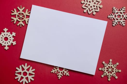Christmas winter festive ornament. Blank paper card with wooden snowflake on red background. Minimal decoration. Invitation Christmas holiday party. Flat lay, top view, copy space.