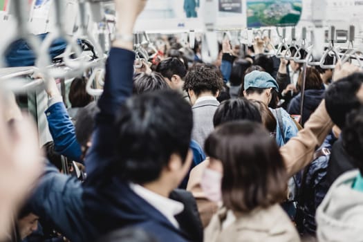 Passengers traveling by Tokyo metro. Business people commuting to work by public transport in rush hour. Shallow depth of field photo. Horizontal composition.