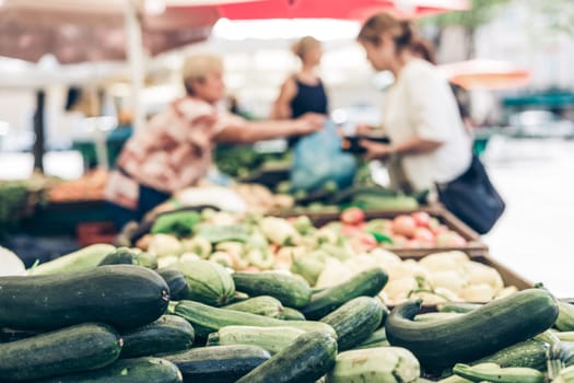 Farmers' food market stall with variety of organic vegetable. Vendor serving and chating with customers.