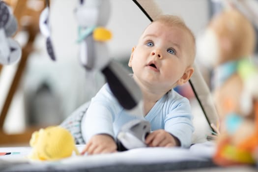 Cute baby boy playing with hanging toys arch on mat at home Baby activity and play center for early infant development. Baby playing at home.