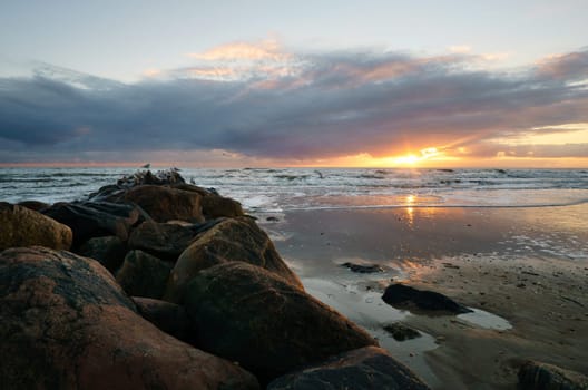 Sunset on the beach in Denmark. Stone groyne in the foreground. Walk on the coast in the sand. Landscape photo by the sea