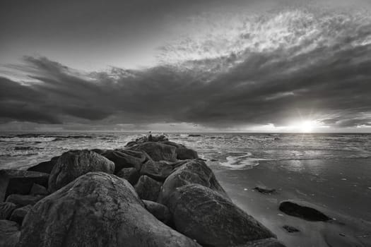 Sunset on the beach in Denmark taken in black and white. Stone groyne in the foreground. Walk on the coast in the sand. Landscape photo by the sea