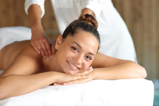 Happy woman receiving a massage in the back in spa looking at camera