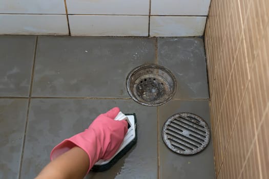 Woman cleaning bathroom floor that is very dirty.