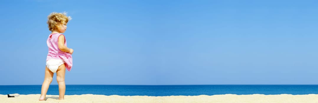 Portrait of blond blue eyed baby having fun on the beach. Banner lots of copy space