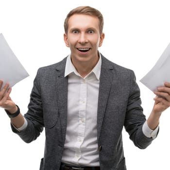A young man in a gray blazer joyfully holds papers in each hand, expressing excitement in a bright studio environment.