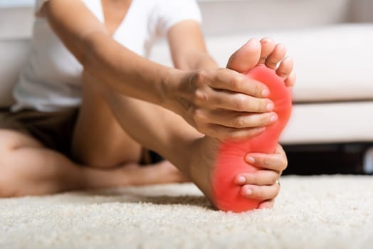 Foot pain, Asian woman feeling pain in her foot at home, female suffering from feet ache use hand massage relax muscle from soles in home interior, Healthcare problems and podiatry medical concept
