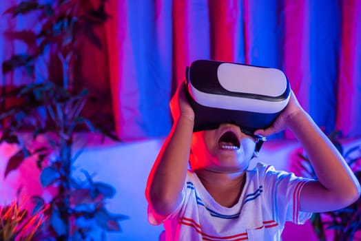 Asian little kid boy wearing virtual reality goggles experiencing reality, Child wear VR helmet excited open mouth at home dark purple and blue background, Virtual technology