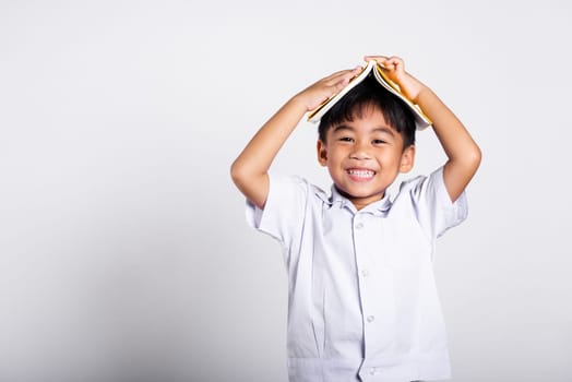 Asian adorable toddler smiling happy wearing student thai uniform red pants stand holding book over head like roof in studio shot isolated on white background, Portrait little children boy preschool