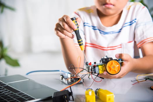 Little child tighten the nut with a screwdriver to assemble car toy, Asian kid boy assembling the Arduino robot car homework project at home, education AI technology workshop school learning lesson