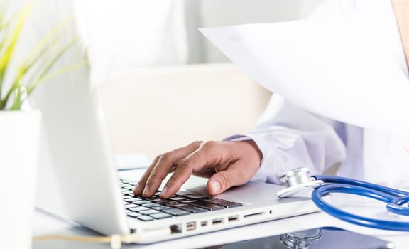 Doctor or nurse woman in uniform with stethoscope working she typing information of patient prescription from paperwork medical history form into laptop computer for record document data report