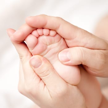 Masseuse massaging little baby girl's foot, shallow focus