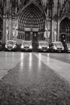 Grayscale shot of row of Mercedes-Benz Sprinter police cars in front of Cologne Cathedral in Germany