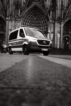 Grayscale shot of Mercedes-Benz Sprinter police car in front of Cologne Cathedral in Germany