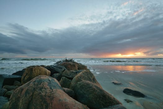 Sunset on the beach in Denmark. Stone groyne in the foreground. Walk on the coast in the sand. Landscape photo by the sea