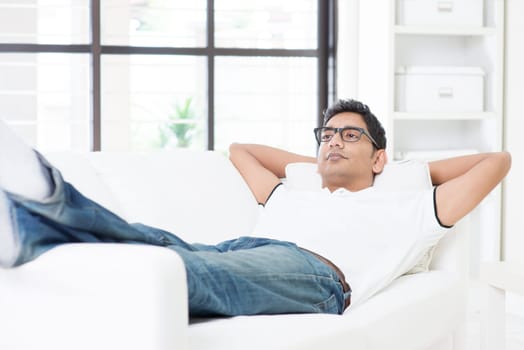 Indian guy resting and daydreaming at home. Asian man relaxed and lying on sofa indoor. Handsome male model.