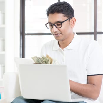 Indian guy counting cash, earning money from his successful internet business. Asian man working from home.
