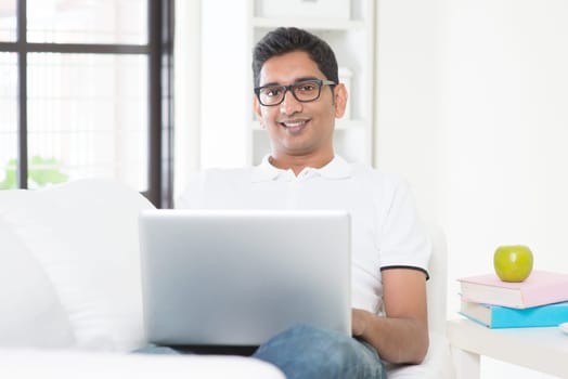 Indian guy with laptop computer working from home. Asian man using internet indoor, relaxed and sitting on sofa. Handsome male model.