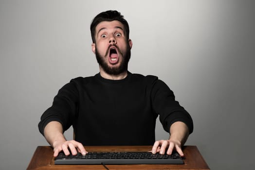 Crazy businessman sitting at table on gray background.  hands on the keyboard