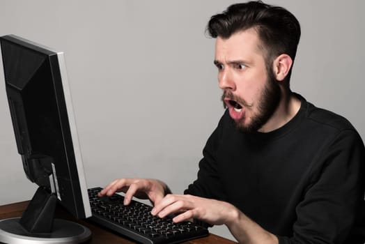 Funny and crazy man using a computer on gray background. man&#39 s hands on the keyboard. Concept of surprise and indignation