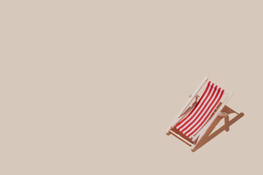 Vacation, beach, travel or relaxation concept. Beige background flat lay as symbol of sand with mini sun lounger for beach chair. Minimalism with copy space area for text, wooden red-white lounge