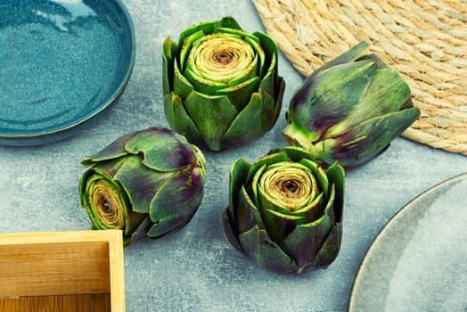 Unopened raw artichoke buds, food on kitchen table. Italian cuisine