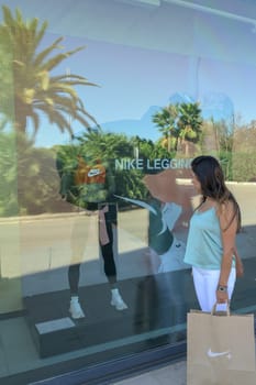 mallorca, balearic islands spain-november 05 2022: hispanic woman in Mallorca Fashion Outlet, looking at showcase of nike sportswear store in mall