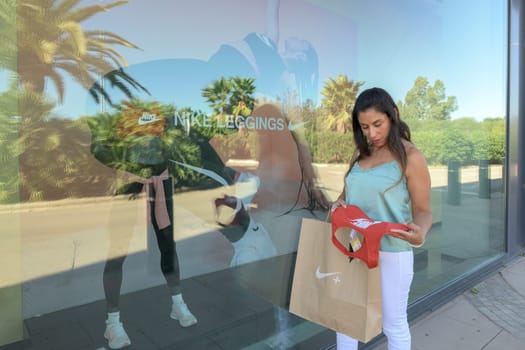 mallorca, balearic islands spain-november 05 2022: hispanic woman looking at the window of the nike sports store happy comparing the purchase made in the mall mallorca fashion outlet, on the outskirts of the city of palma