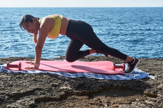 FITNESS WOMAN IN SPORTS SET TRAINING WITH ELASTIC BAND, WEIGHTS, GYM EXERCISES, IN FRONT OF THE WATER.