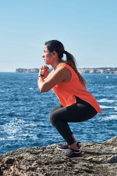 FITNESS WOMAN IN SPORTS SET TRAINING WITH ELASTIC BAND, WEIGHTS, GYM EXERCISES, IN FRONT OF THE WATER.