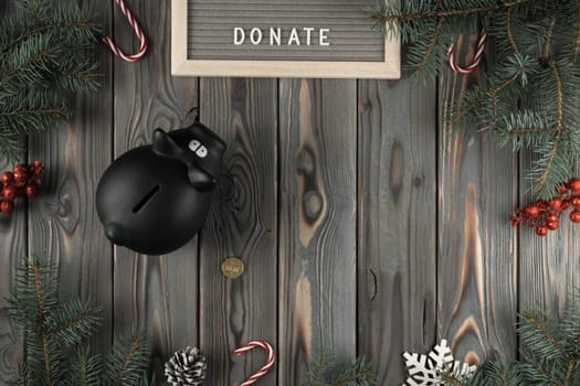 Abstract holiday composition with black pig moneybox with golden coin in Christmas twigs and candies decoration. Charity, donation and altruism. Generosity in holidays. Flat lay, copy space, mockup