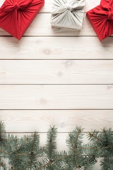 Vertical composition of natural, handmade, festive red and white Furoshiki present boxes with decorated spruce twigs on wooden background. Greeting card, wallpaper frame. Flat lay, copy space