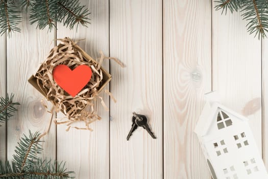 Open wrapping paper box with red heart present and metallic key with house model in pine tee twigs decoration on wooden view. Moving apartment, mortgage, lucky purchase. Flat lay, top view, copy space