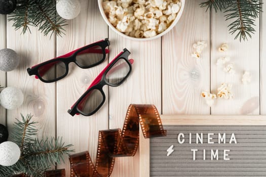 Abstract cinema time composition frame of popcorn bucket, 3d glasses, film, fir twigs, garland on wooden background. Time to watch movies, premier and modern 3d technology. Flat lay, copy space