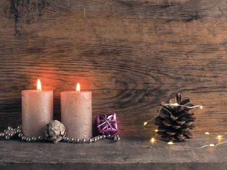 Candle of the second Advent burns, pine cones and Christmas decoration on wood with Christmas lights