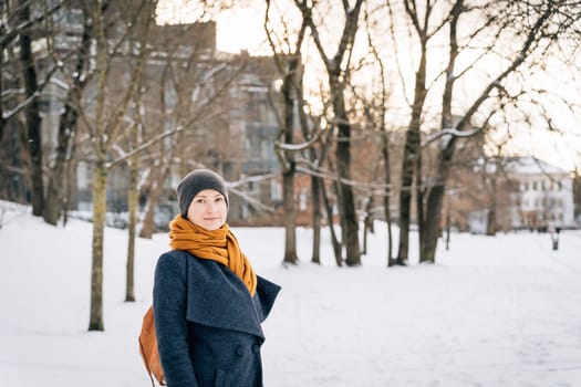 A woman on the street of a winter city looks into the camera.