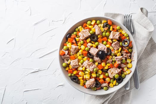 Healthy tuna salad with corns, carrots, peas and olives on white table background. Mexican corn salad.