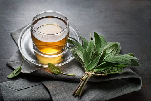 Sage tea in glass mug and sage leaves on grey table close up