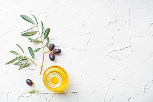 Olive oil in bowl with fresh olives fruit and olive branch on white background close up