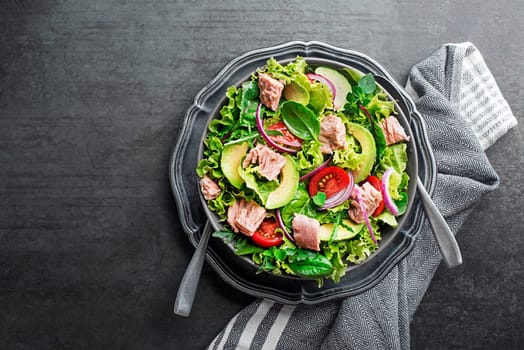 Fresh green leafy salad with tuna avocado and tomato on grey table background. Concept for a tasty and healthy meal