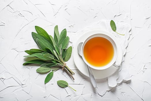 Sage tea in white cup and sage leaves on white table close up
