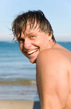 Handsome sexy forties man smiles at the camera as he enjoys a summer`s day on the beach.